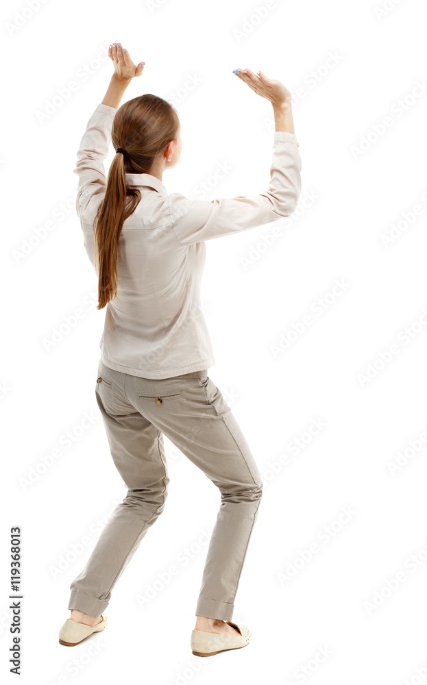 back view of woman protects hands from what is falling from above. Isolated over white background. Skinny girl in white denim suit holding a load over your head. back view of woman protects hands from what is falling from above. Isolated over white background. Skinny girl in white denim suit holding a load over your head.