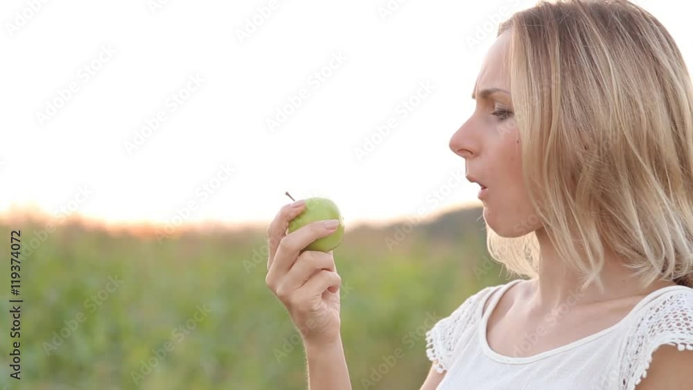 Caucasian woman with a toothpain sitting on a park bench and eating green apple Caucasian woman with a toothpain sitting on a park bench and eating green apple