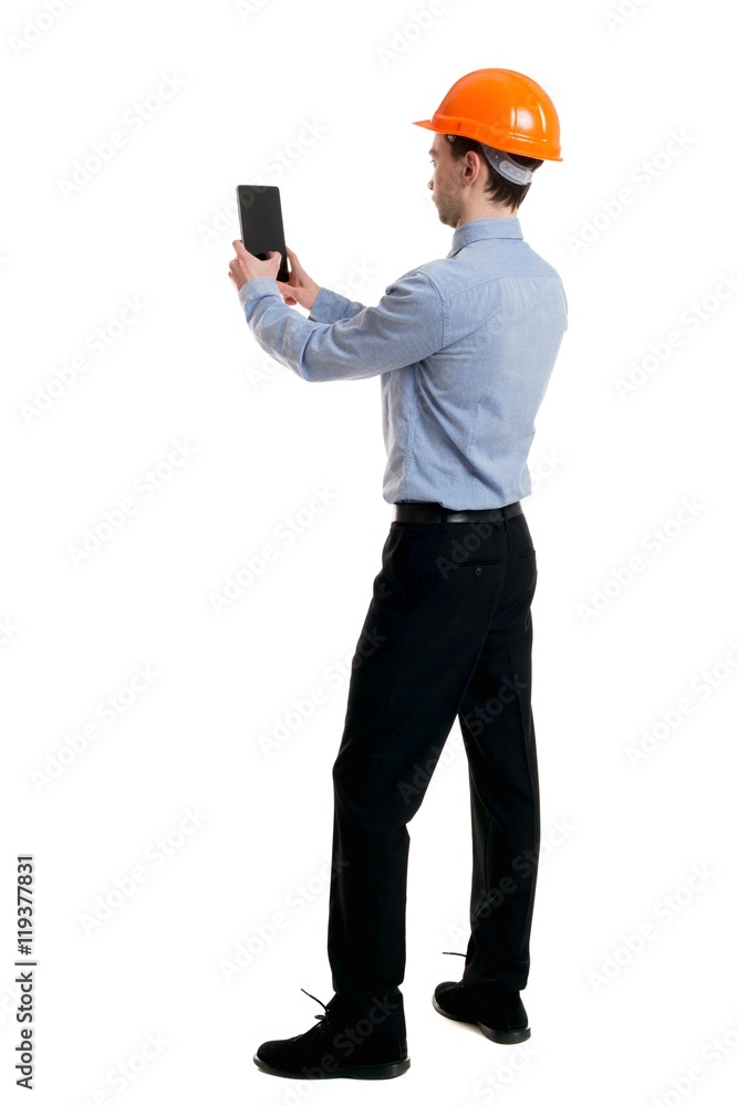 Backview of business man in construction helmet stands and enjoys tablet or using a mobile phone. Curly businessman in a light jacket and a helmet makes selfie tablet. Backview of business man in construction helmet stands and enjoys tablet or using a mobile phone. Curly businessman in a light jacket and a helmet makes selfie tablet.