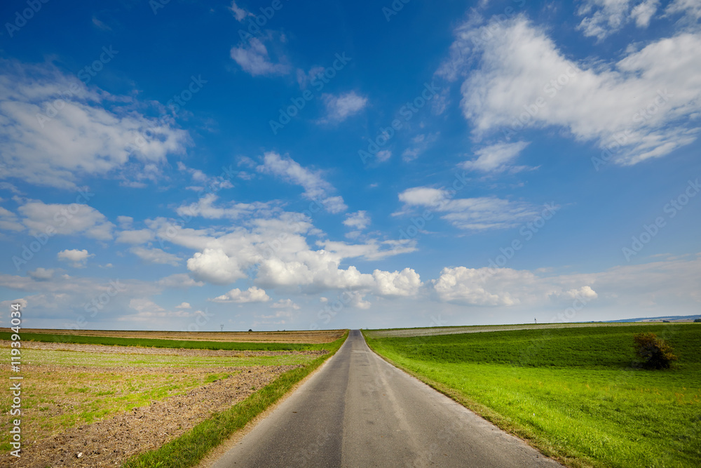 asphalt road through the green field and clouds on blue sky in s