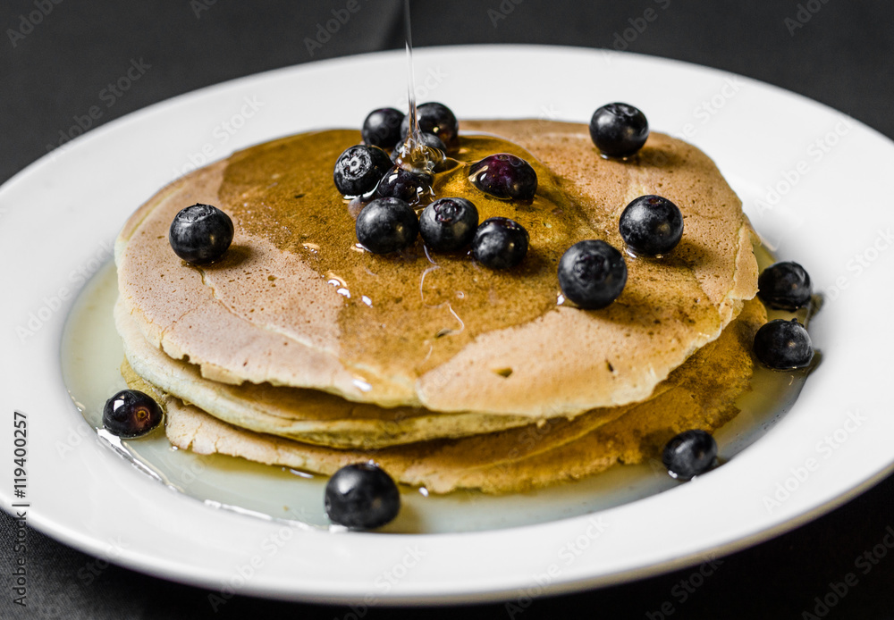 Close up of a bunch of tasty american pancakes with colorful blueberries and maple syrup poured over them. Selective focus. Close up of a bunch of tasty american pancakes with colorful blueberries and maple syrup poured over them. Selective focus.