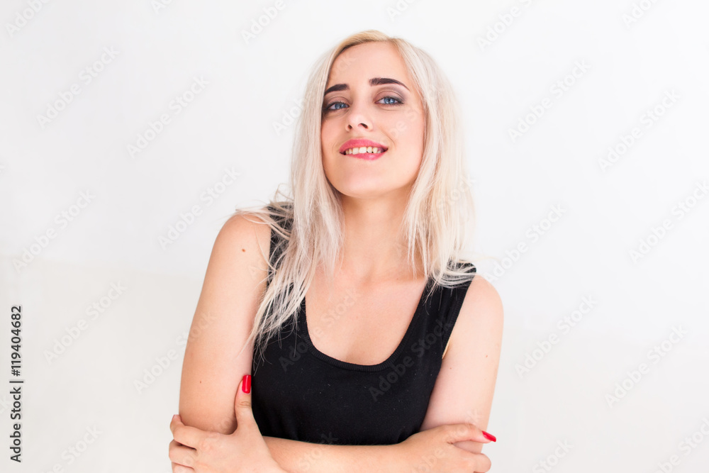 Confident beautiful woman in black dress biting her lip. Young attractive blonde with folded arms looking at camera with arrogant expression, white background Confident beautiful woman in black dress biting her lip. Young attractive blonde with folded arms looking at camera with arrogant expression, white background