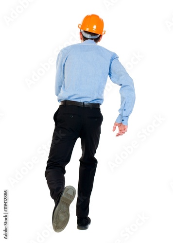 Back view of running engineer in helmet. Businessman in a blue shirt and a helmet in a hurry to call.