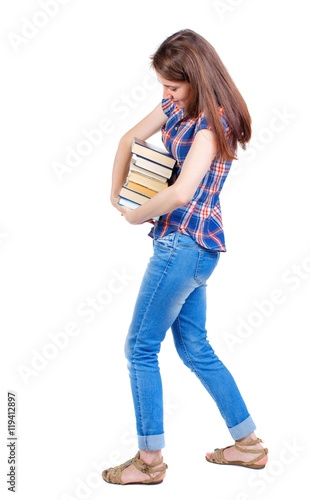 Girl carries a heavy pile of books. back view. Girl in plaid shirt trying more convenient to pick up a stack of books.