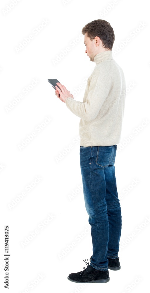 back view of business man uses mobile phone. Curly short-haired man in a woolen white jacket standing sideways and leafing through an e-book. back view of business man uses mobile phone. Curly short-haired man in a woolen white jacket standing sideways and leafing through an e-book.