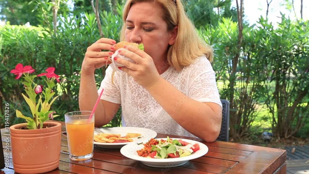 Middle aged woman in white shirt and long blond hair eating a fast food at table in restaurant Middle aged woman in white shirt and long blond hair eating a fast food at table in restaurant