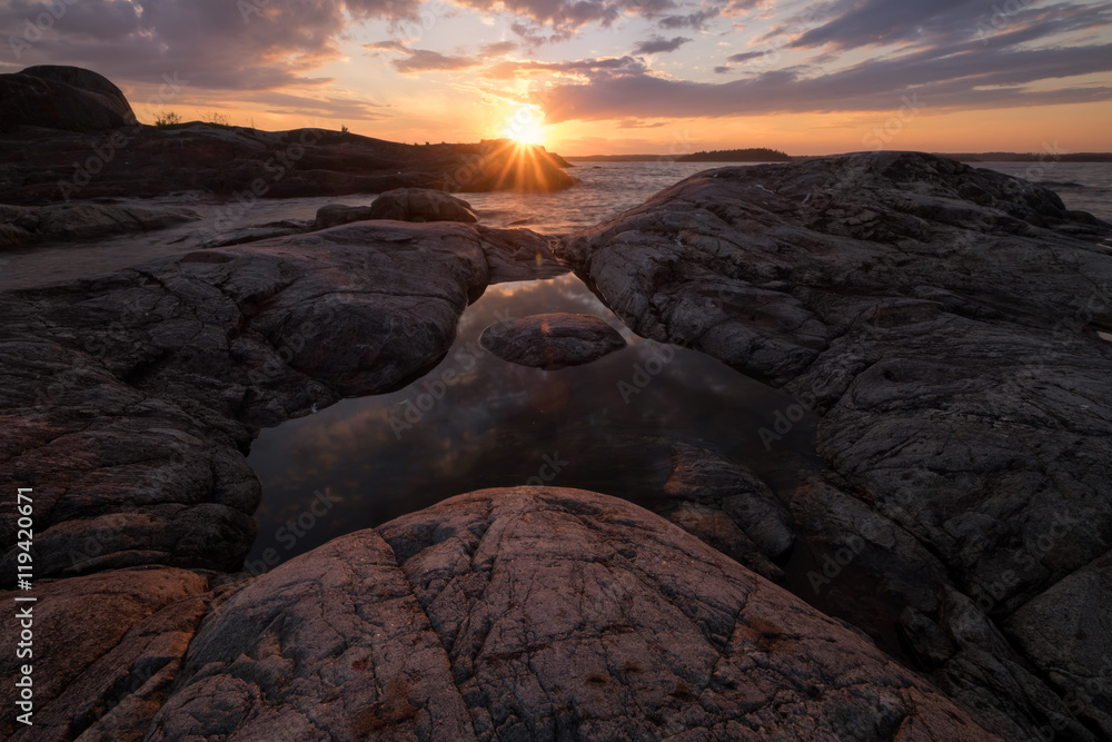 The rays of the setting sun glows the cracks in the granite rocks that surround a small pond in shape of triangle on the island Taakionluodot, Russia, Karelia
