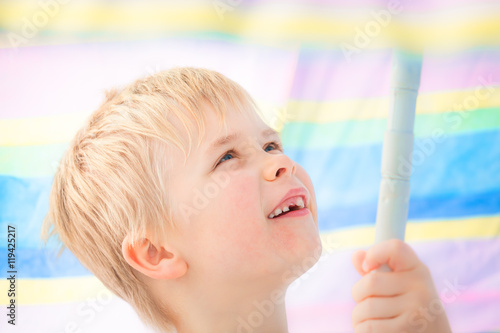 Enjoy Under the Parasol / Cute child boy at school age with missing milk tooth smiling under pastel colored sunshade umbrella photo