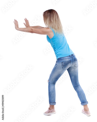back view of woman pushes wall. Isolated over white background. blonde in a blue shirt and jeans, put her hands on the wall.