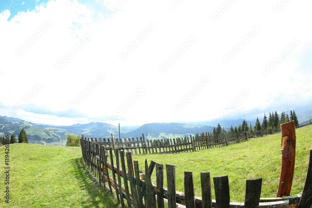 Fototapeta premium Wooden fence on green hills in mountains