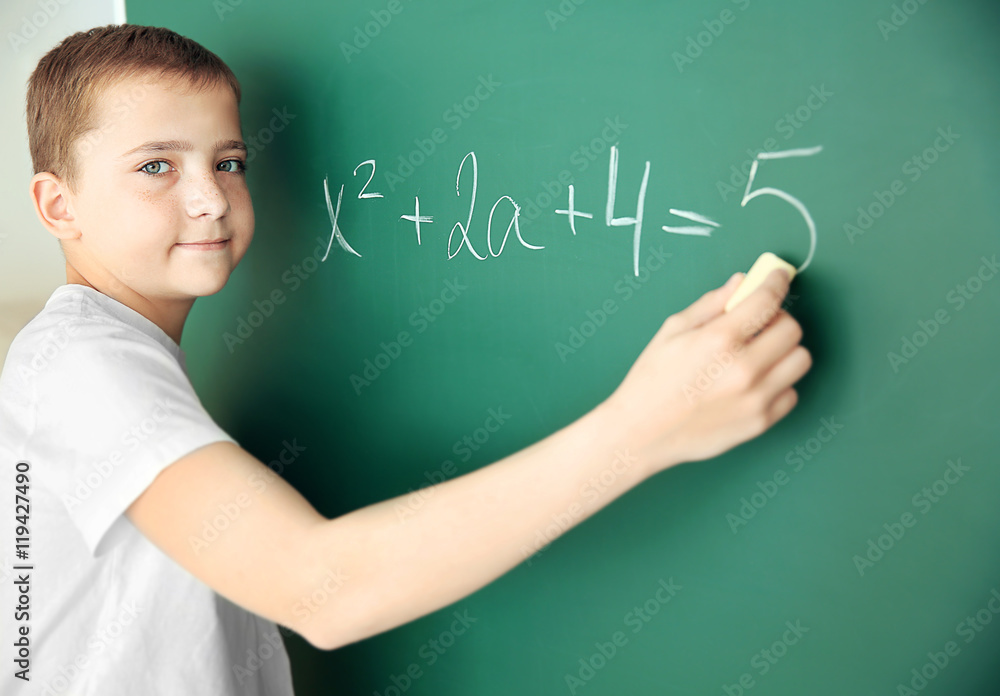 Cute schoolboy writing on chalkboard