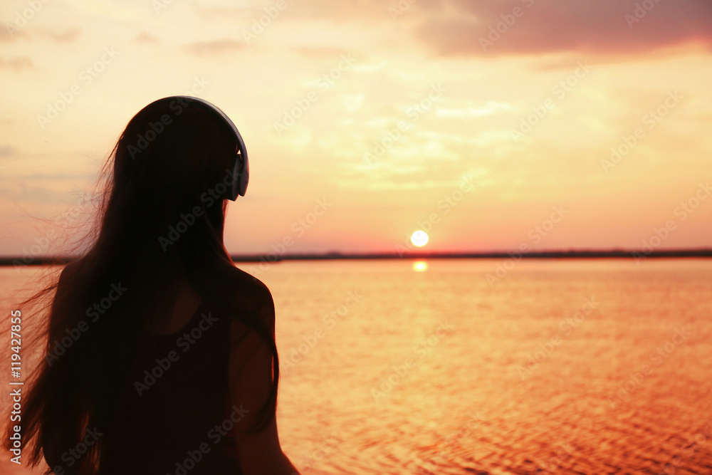 Silhouette of woman with headphones on sunset sky background