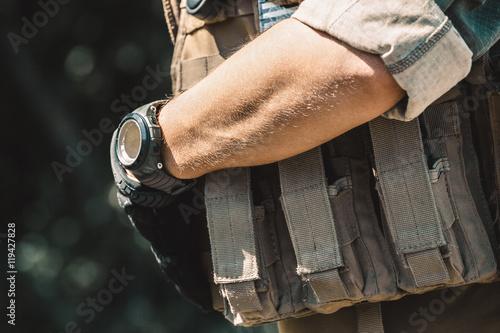 Male soldier wearing a bulletproof vest and a shirt with short sleeves. On hand watches.