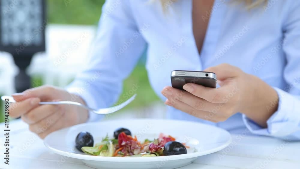 Beautiful woman using smartphone and eating salad in cafe in city Beautiful woman using smartphone and eating salad in cafe in city