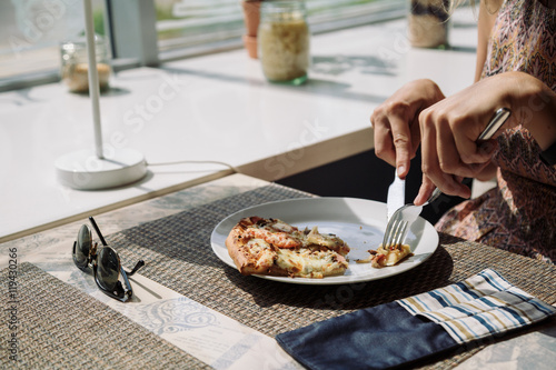 close-up of unrecognizable woman holding slice of delicious pizza with glass of cold brew coffee in sunlight