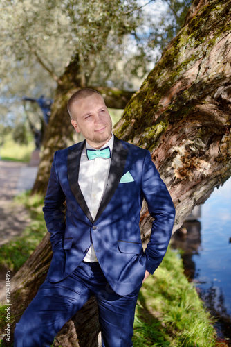 Handsome groom in suit in the nature. Male portrait in the park. Beautiful model boy in colorful wedding clothes. Man is posing. Handsome guy outdoors