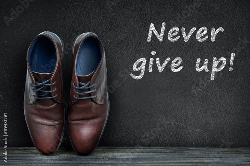 Never give up text on black board and business shoes