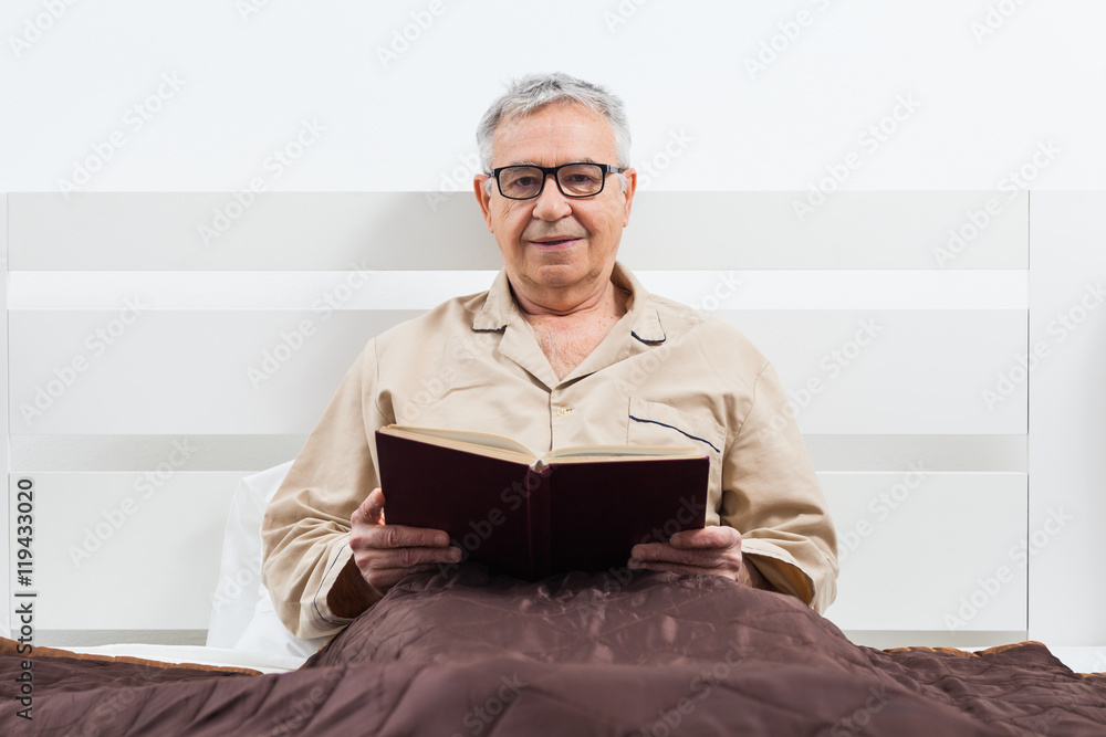 Senior man is lying in bed and reading a book before sleep. Senior man is lying in bed and reading a book before sleep.