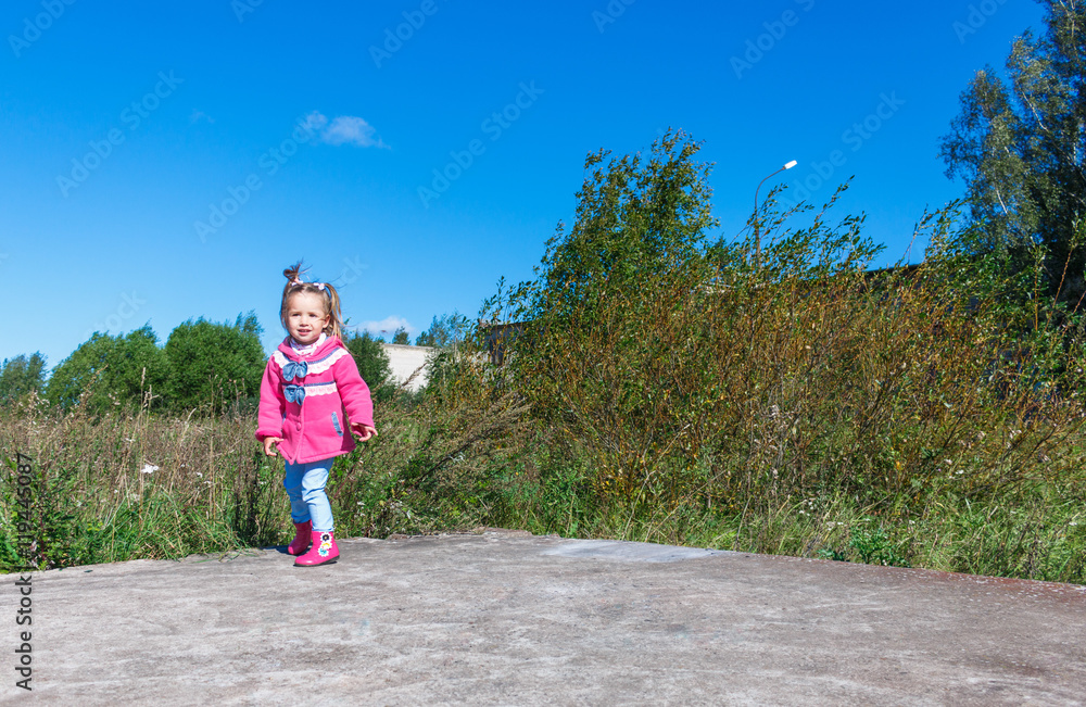 Little girl in a pink coat, jeans and boots walking the park Little girl in a pink coat, jeans and boots walking the park