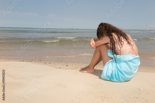 Sad little girl sitting on the beach. Place for text.