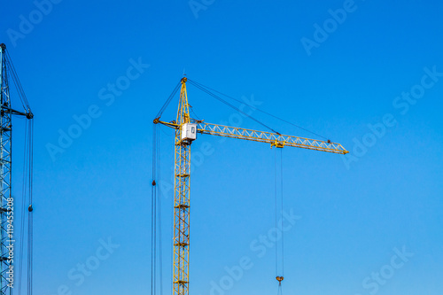 Crane against the blue sky. Yellow crane at the construction site.