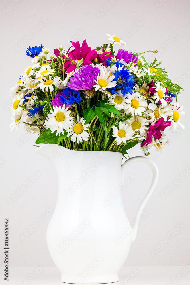 Wildflowers in white ceramic jug. Wild flower bouquet on white table