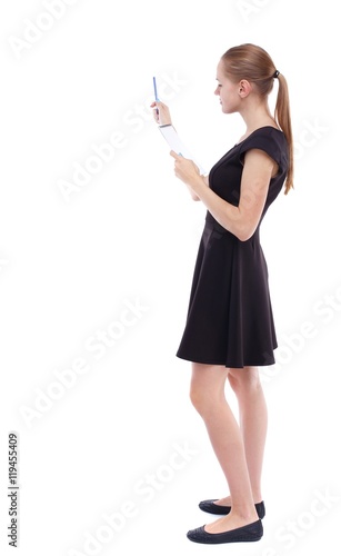 back view of stands woman takes notes in a notebook. girl watching. Isolated over white background. Blonde in a short black dress check the records in a notebook.