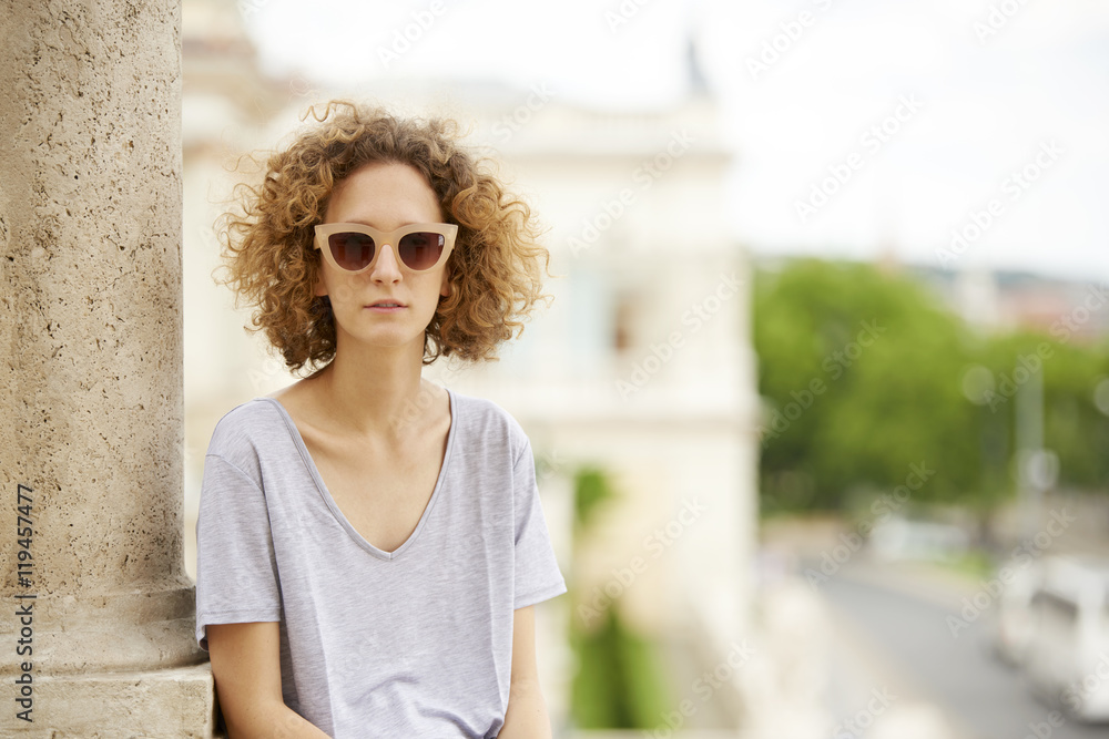 Summer day in the city. Close-up portrait of young confident woman wearing sunglasses and smiling. Summer day in the city. Close-up portrait of young confident woman wearing sunglasses and smiling.