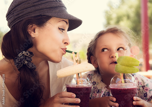 Friendly kid girl and fun emotional mother drinking berries smoo photo