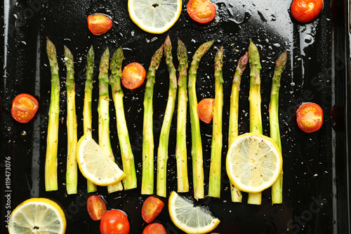 Fresh baked asparagus with lemons and tomatoes on black pan