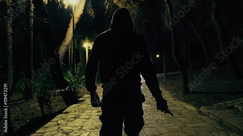 Hooded man walks in dark park draws knide,slomo 100p