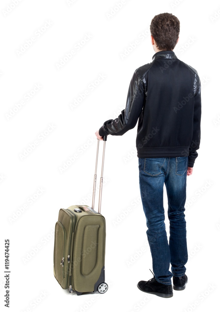 Back view of man with green suitcase looking up. Curly short-haired guy in a black jacket standing with green suitcase. Back view of man with green suitcase looking up. Curly short-haired guy in a black jacket standing with green suitcase.