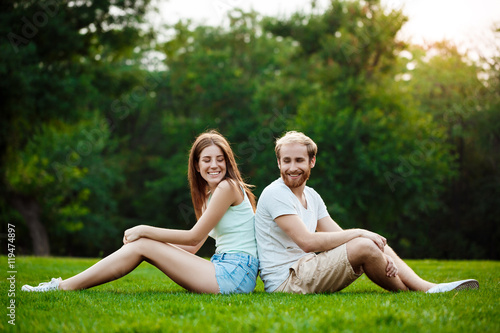 Young beautiful couple smiling, sitting on grass in park. Outdoor background.