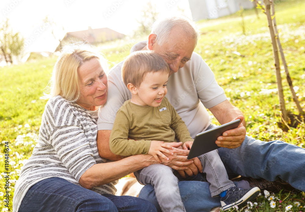 Grandparents with grandson enjoying the sunny spring day outdoors. They are looking something on tablet. Grandparents with grandson enjoying the sunny spring day outdoors. They are looking something on tablet.