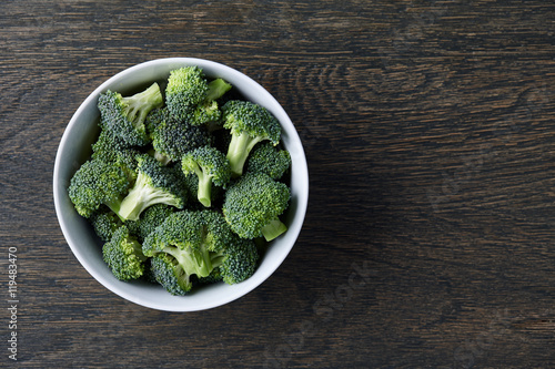 Fresh green broccoli in a white bowl on dark wooden background, top view