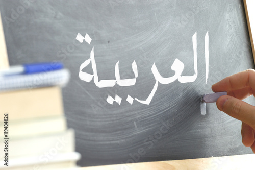 Hand writing on a blackboard in an Arabic class. Some books and school materials. photo