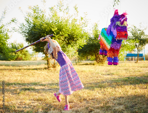 Wall Mural Young girl at an outdoor party hitting a pinata