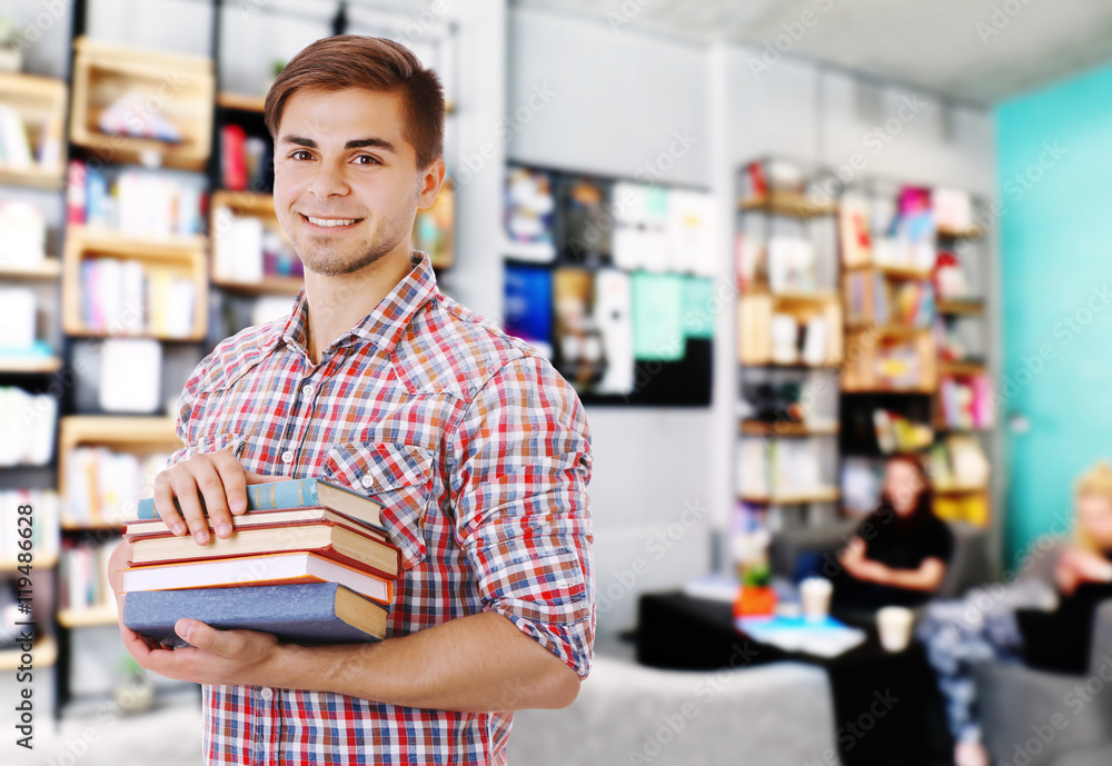 Young man with stack of books on blurred book shelves background. Young man with stack of books on blurred book shelves background.