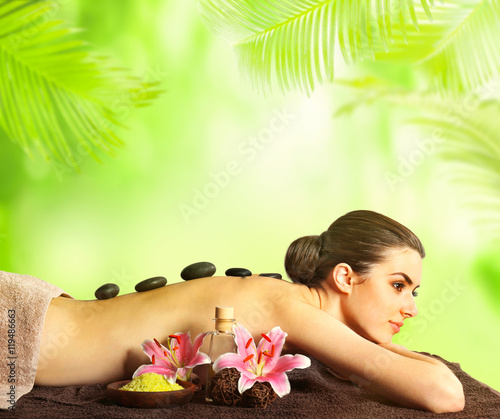 Spa concept. Beautiful woman lying on massage table. Blurred green palm leaves background.
