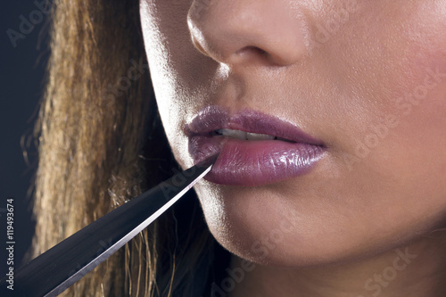 Knife tip pressing the lower lip of a serious latin woman. Close up, shallow deep of field, focus on her lips.