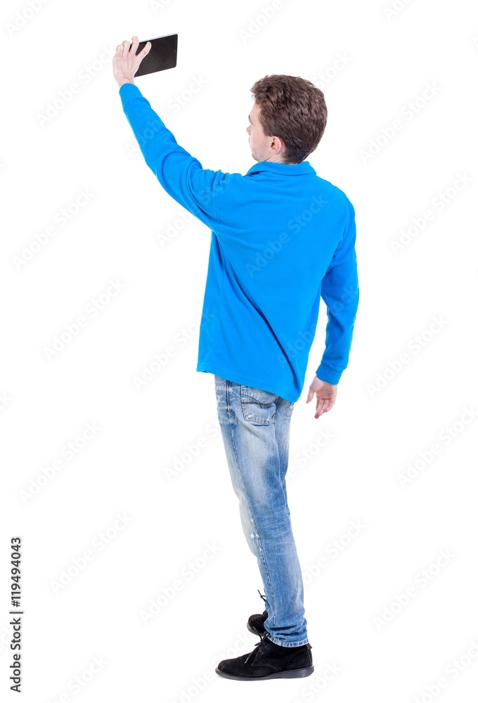 back view of standing business man photographing a phone or tablet. Curly boy in blue sweater makes selfie tablet. back view of standing business man photographing a phone or tablet. Curly boy in blue sweater makes selfie tablet.
