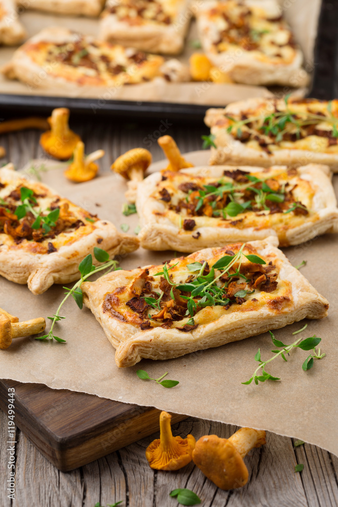 Homemade tarts of puff pastry with seasonal chanterelle mushrooms, cheese, thyme and onion on rustic wooden table, selective focus