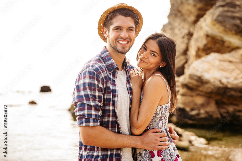 Happy young hipster couple standing at the beach and hugging Happy young hipster couple standing at the beach and hugging