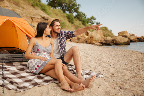 Man pointing at something while sitting with girlfriend on beach