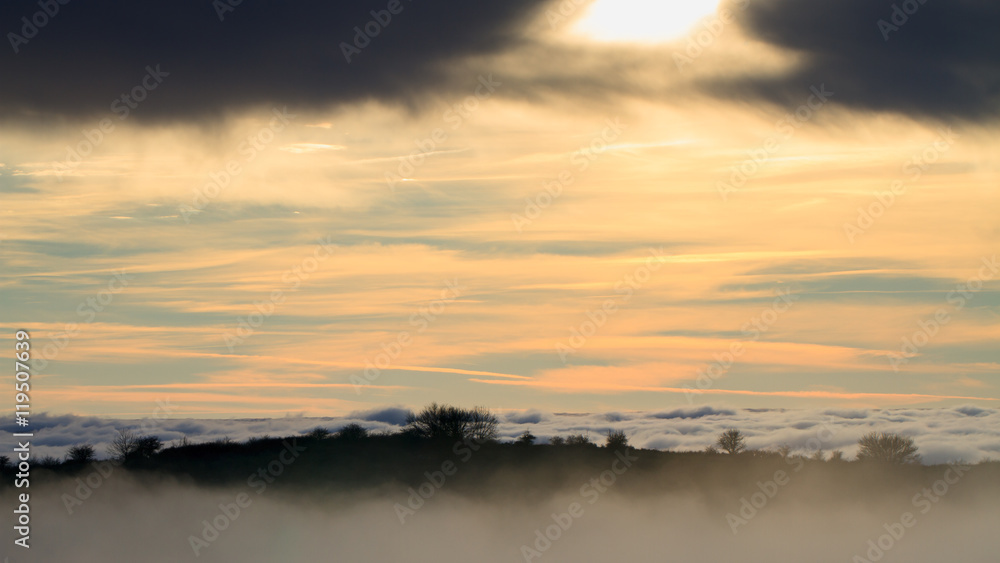 Fototapeta premium Landscape with the sun setting behind clouds and fog