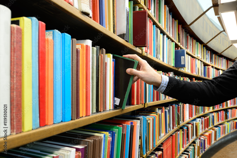 Naklejka premium Hand picking book in library bookshelf