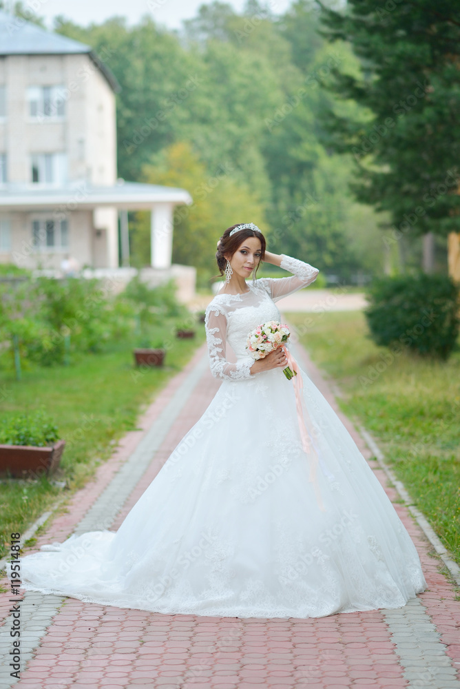 Young beautiful happy bride with flower bouquet in park