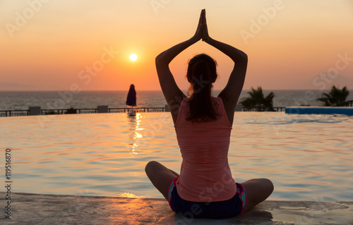 Frau praktiziert yoga am infinity pool bei Sonnenuntergang