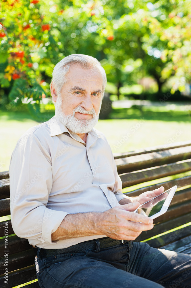Senior man using digital tablet in a park, active lifestyle concept Senior man using digital tablet in a park, active lifestyle concept
