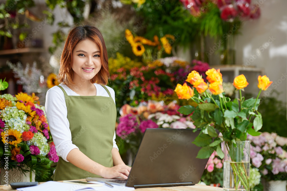 Portrait of cheerful Vietnamese florist working on laptop